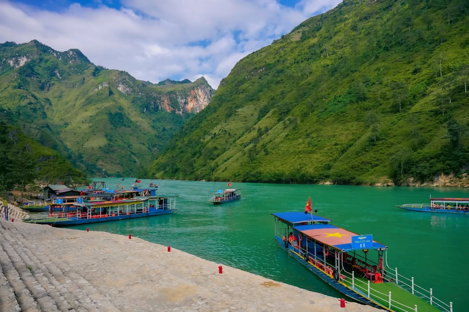 Colorful boats dock on the turquoise Nho Que River between towering green mountains in Ha Giang.