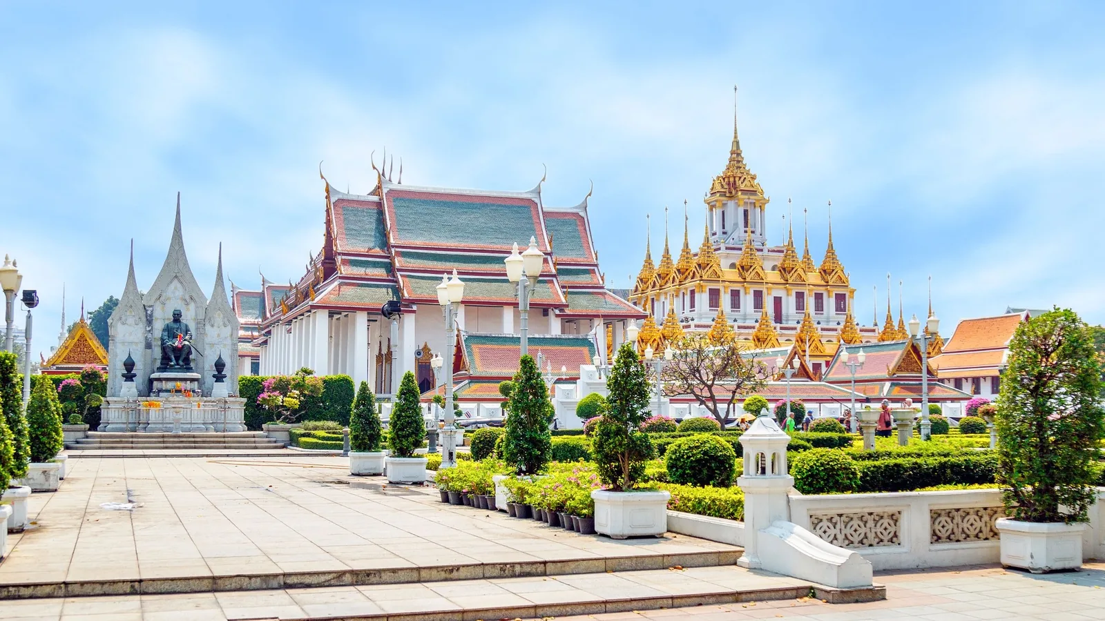 Ornate spires and multi-tiered roofs of a Buddhist temple complex rise above manicured gardens in Bangkok