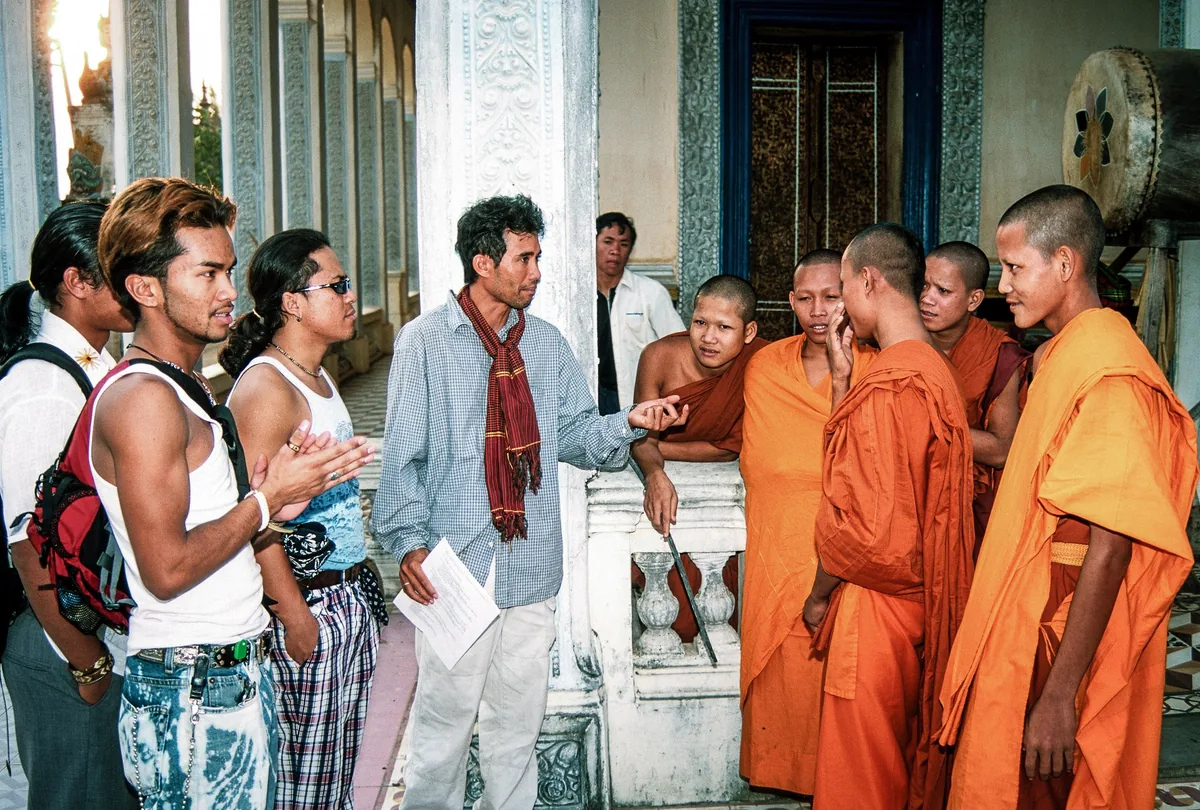 Visitors chat with young Buddhist monks in orange robes on a temple veranda in Siem Reap.