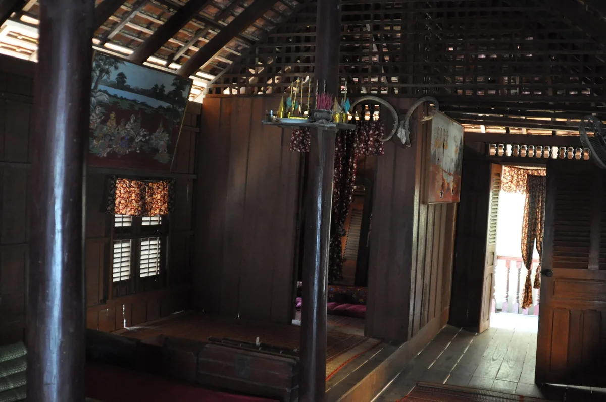 Wooden interior of a traditional Khmer stilt house with a small altar and open door leading to a bright veranda in Phnom.