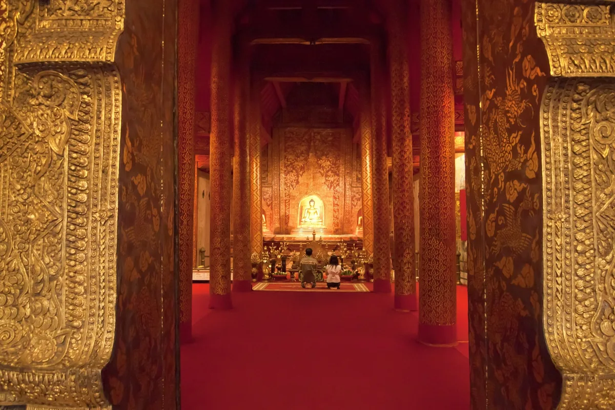 Worshippers kneel before a golden Buddha statue inside the ornately gilded hall of Wat Phra Singh in Chiang Mai.