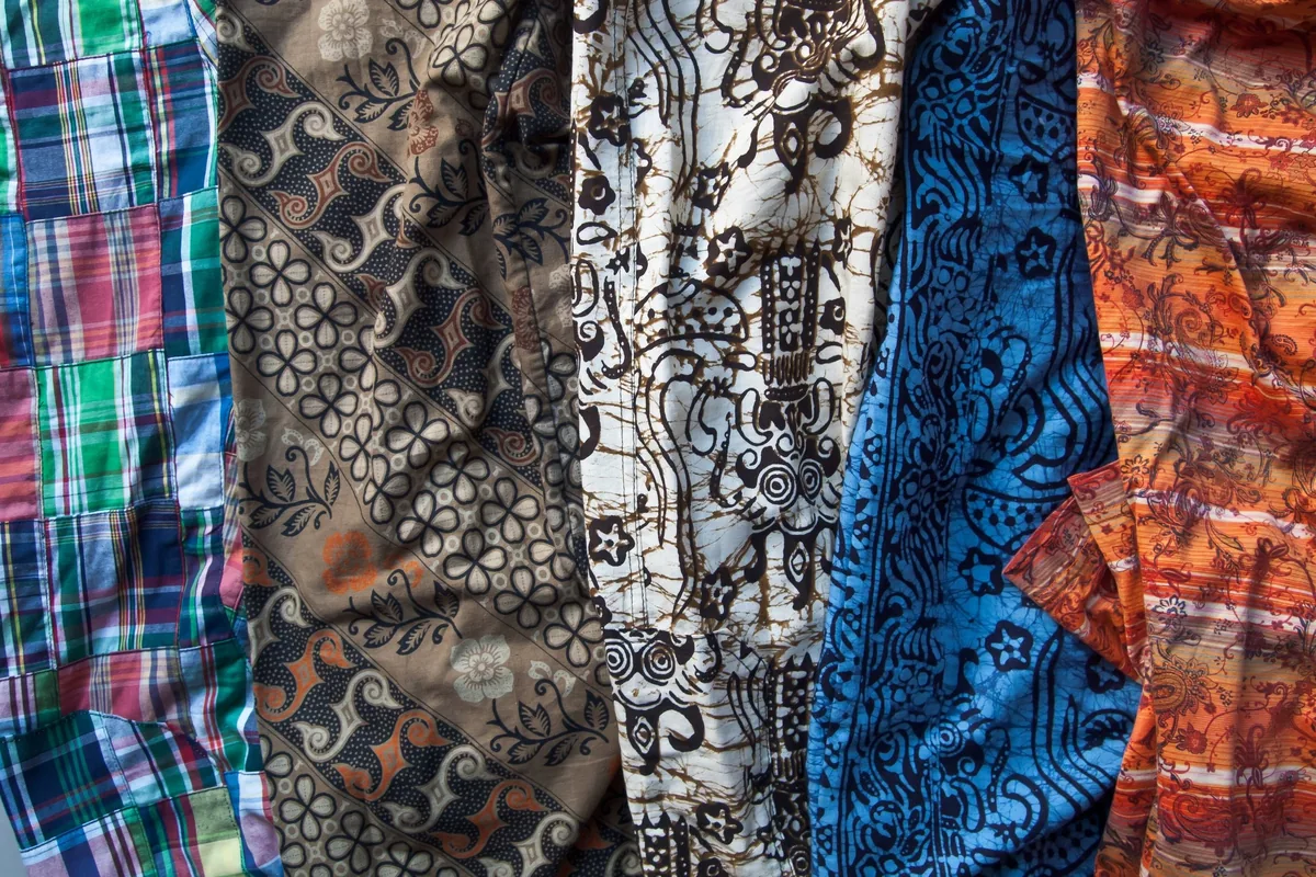 Colorful patterned fabrics and batik-style clothing hang side by side at a market in Chiang Mai.