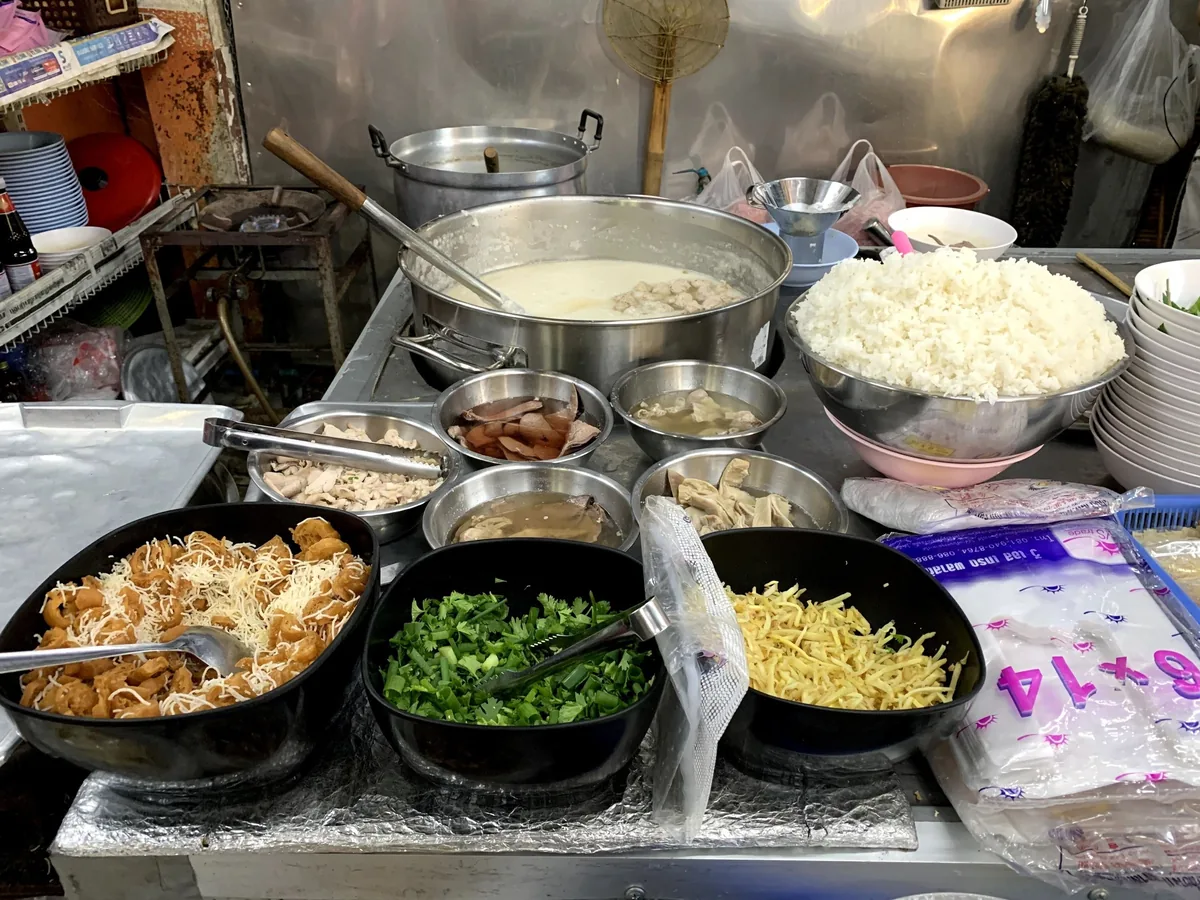 A street food stall in Chiang Mai displays bowls of congee toppings and rice beside a pot of rice porridge.