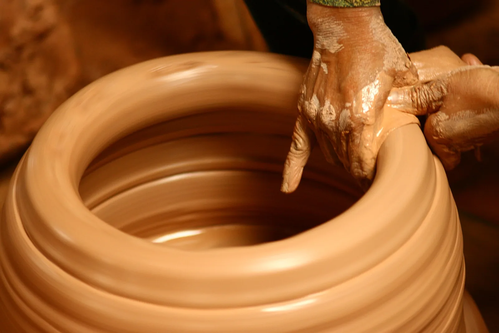 A potter's clay-covered hands shape a spinning clay pot on a wheel near Hanoi.