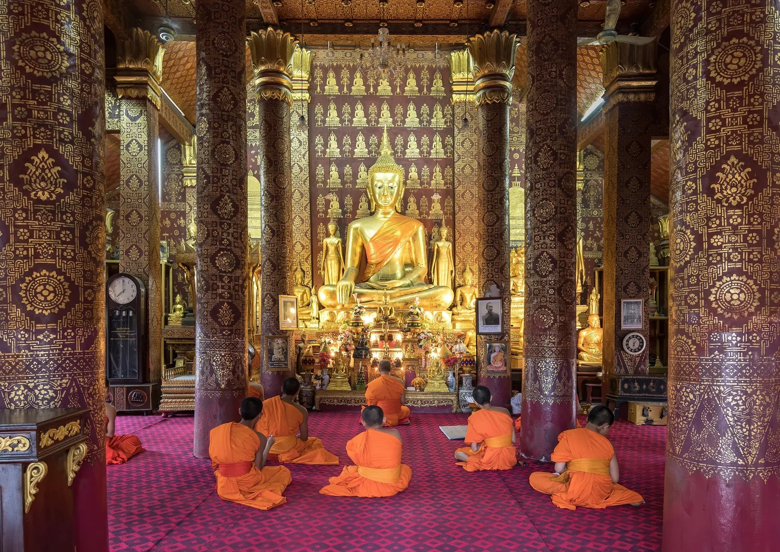 Buddhist monks in orange robes pray before a golden Buddha statue inside a temple in Luang Prabang.