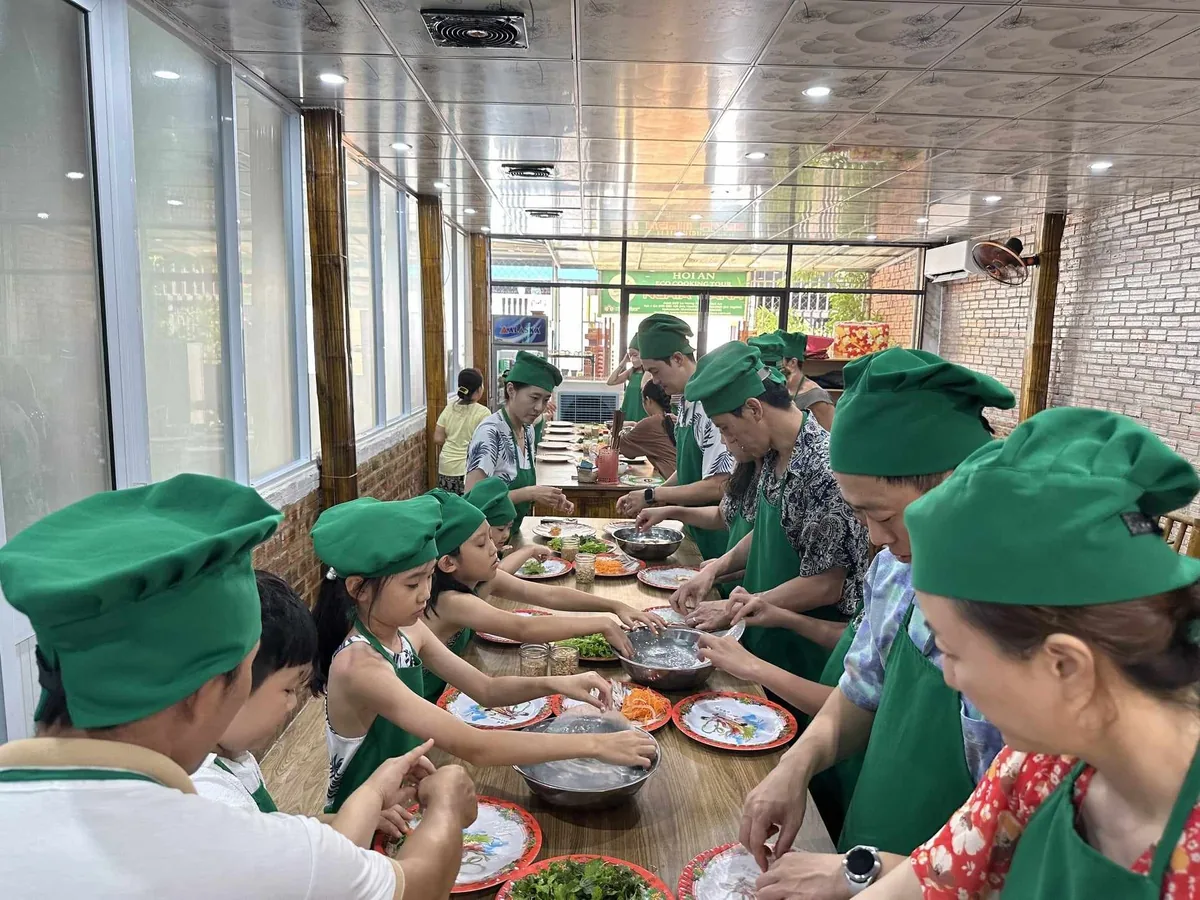 Families in green chef hats prepare fresh spring rolls together at a cooking class in Hoi An.