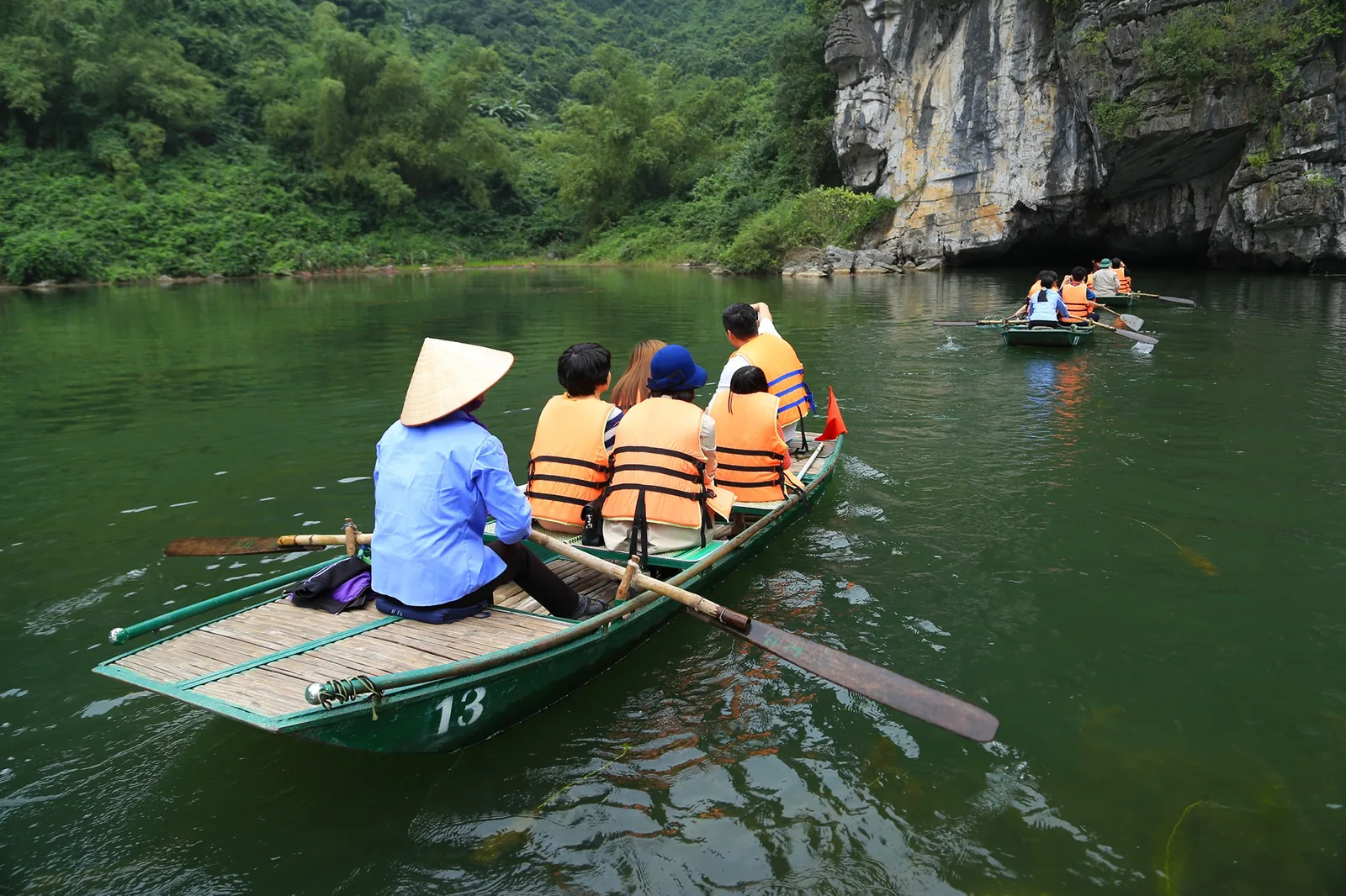 Tourists in life jackets ride a rowboat through a river toward limestone karst caves in Ninh Binh.