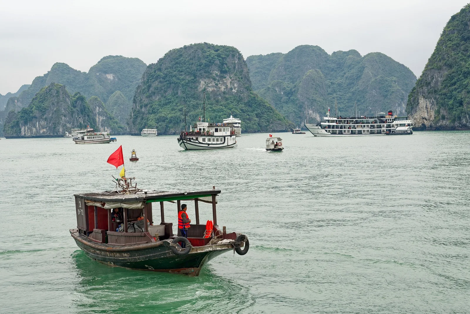 Wooden boats and cruise ships dot the water beneath limestone karsts in Ha Long Bay.