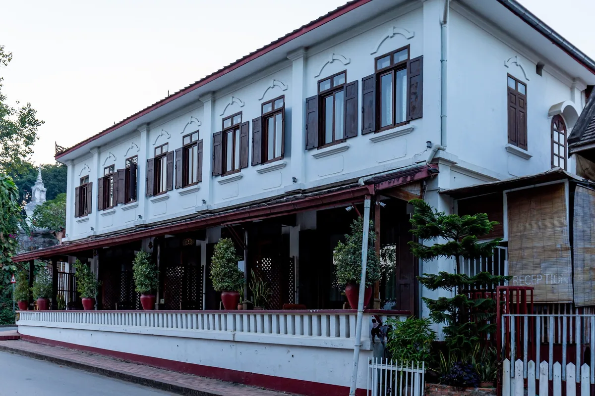 A colonial-era white building with dark shutters and a wooden veranda lines a street in Luang Prabang.