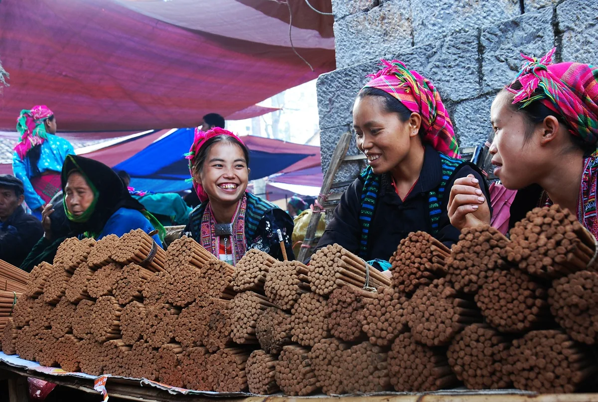 Flower Hmong women in colorful headscarves smile while selling incense sticks at Dong Van market in Ha Giang.