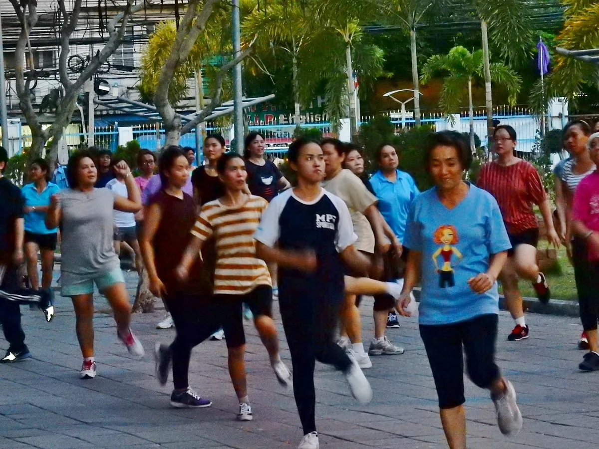 A group of people take part in an outdoor morning exercise class in a Bangkok park.