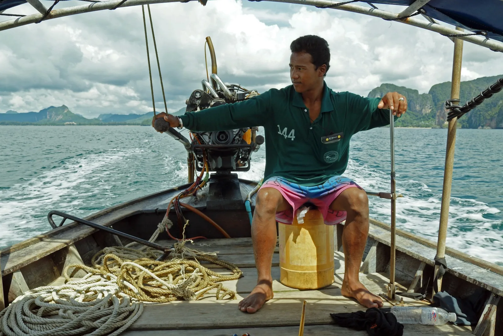 A boatman steers a traditional long-tail boat across the sea near Krabi, limestone cliffs rising in the distance.