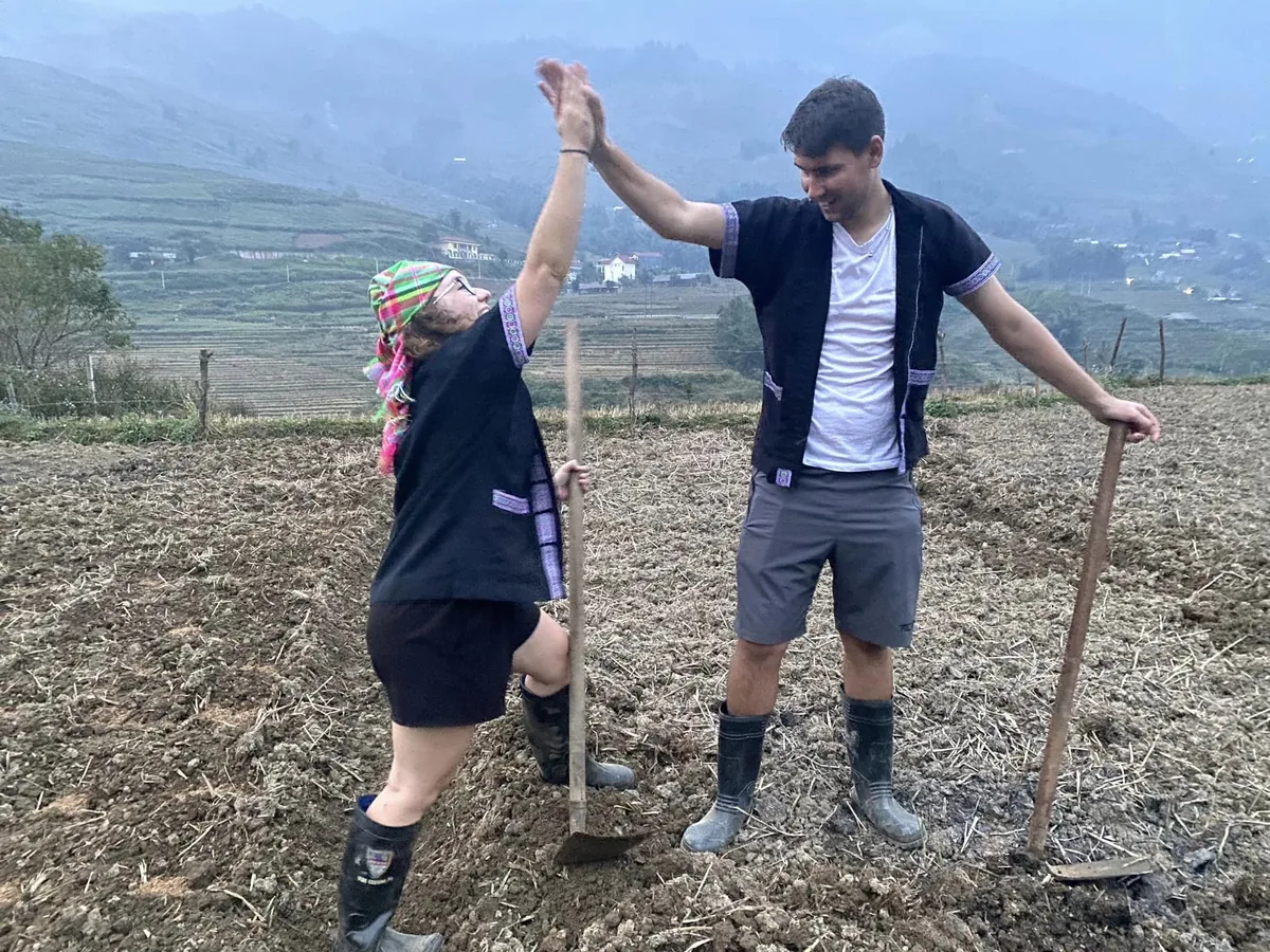 Tourists high-five while working a plowed field in the terraced mountains near Fansipan, Lao Cai.