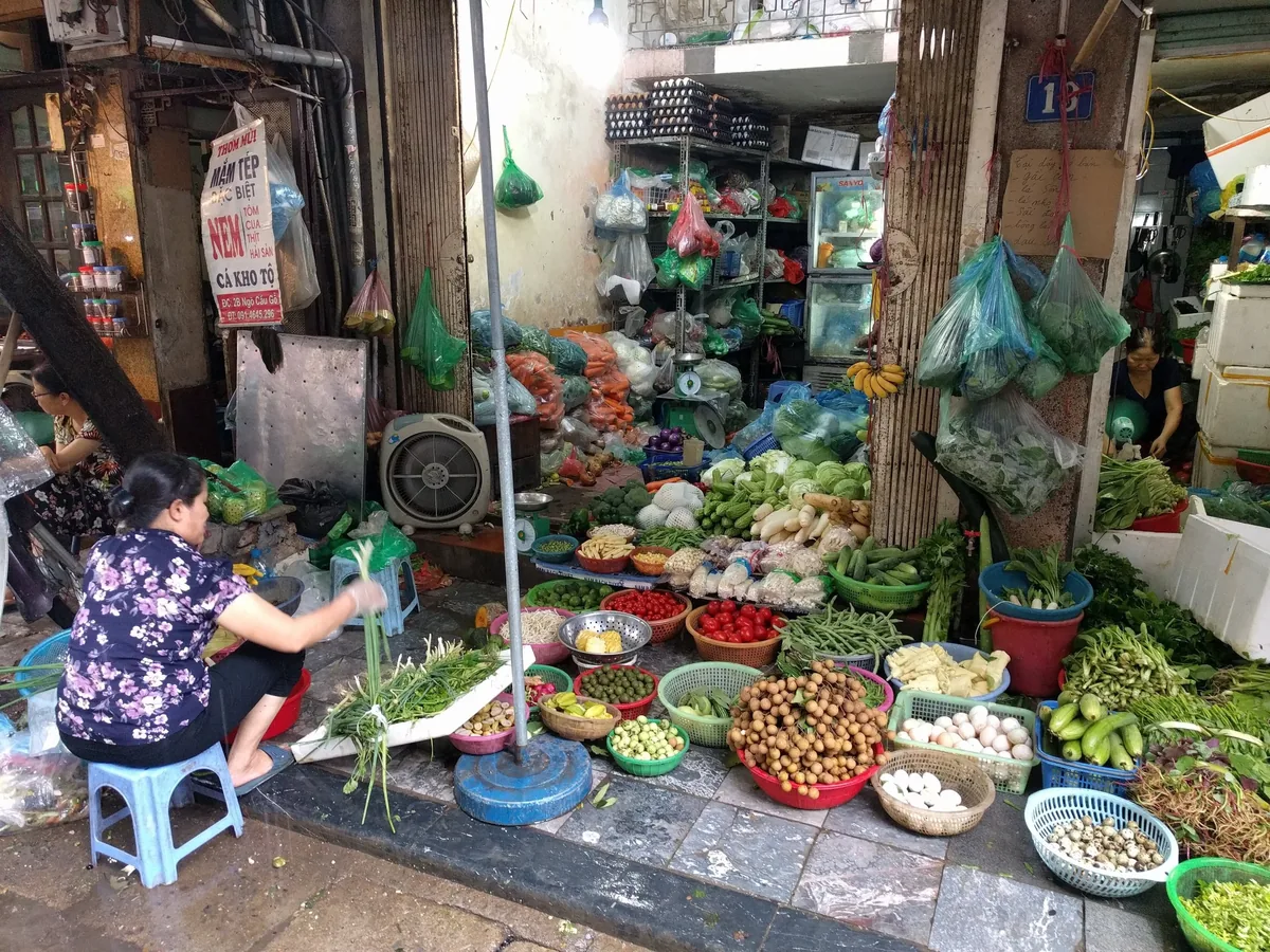 A vendor sorts fresh vegetables amid baskets of produce at a busy street market in Hanoi.