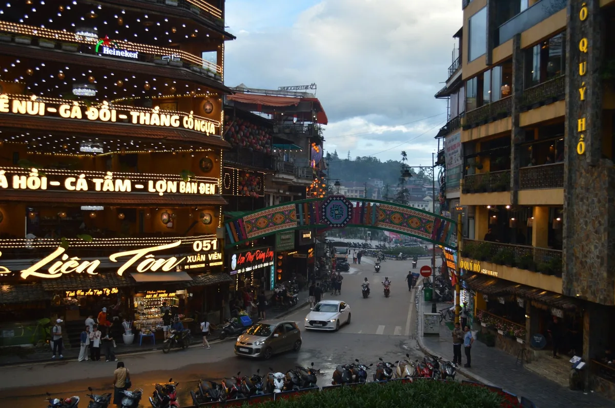 Illuminated restaurant signs and decorative arch line a bustling evening street in Sapa, Vietnam.